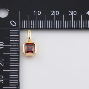 K&ouml;nnte beinhalten: Ein goldfarbener Anh&auml;nger mit einem quadratischen, tiefroten Edelstein. Der Edelstein ist in eine goldene L&uuml;nette gefasst. Der Anh&auml;nger hat eine kleine Schlaufe f&uuml;r eine Kette. Der Anh&auml;nger wird neben einem Lineal gezeigt.