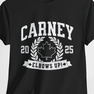 May include: Black t-shirt with white text that reads "CARNEY 20 25 ELBOWS UP!" with a white maple leaf graphic in a wreath.