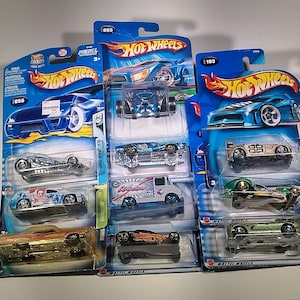 Op de afbeelding: Een verzameling Hot Wheels speelgoedauto's in hun originele verpakking. De auto's zijn in verschillende kleuren, waaronder blauw, zilver, goud en groen. De verpakking toont het Hot Wheels-logo en modelnummers.