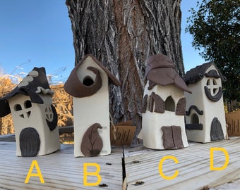 Peut inclure: Quatre nichoirs en céramique faits à la main avec des designs uniques. Chaque maison a une base blanche avec des accents marron, y compris les toits, les portes et les éléments décoratifs. Les nichoirs sont étiquetés A, B, C et D, présentant leurs styles individuels.