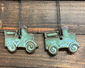 Peut inclure: Deux ornements en céramique bleu sarcelle en forme de voitures anciennes avec des cordons de suspension noirs.