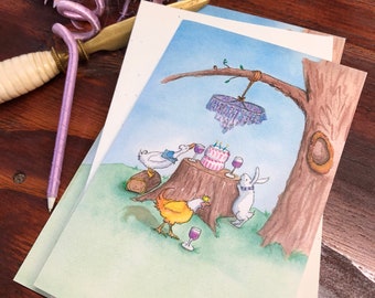 Peut inclure: Cartes de vœux avec une illustration à l'aquarelle d'une fête dans les bois. Un gâteau est posé sur une souche d'arbre, entouré de personnages animaux. Un stylo et une baguette violets avec une décoration en forme d'étoile sont également visibles.