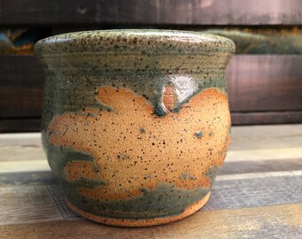 Peut inclure: Mug en céramique fait à la main avec un design tacheté et terreux. La base est de couleur beige avec des accents marron et verts. Le bord est vert foncé, et l'esthétique générale est rustique et organique. Une pièce unique pour savourer des boissons.