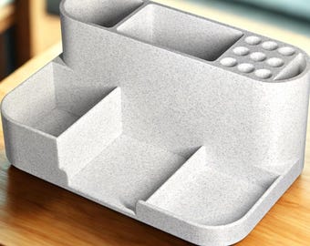 May include: A light gray desk organizer with multiple compartments and a textured surface. It features sections for pens, small items, and a phone or tablet. The organizer sits on a wooden desk.