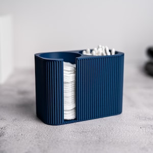 Op de afbeelding: Een marineblauwe organizer met geribbelde textuur voor badkamerbenodigdheden. Het heeft compartimenten voor wattenschijfjes, wattenstaafjes en een cirkelvormig gedeelte. Het ontwerp is modern en minimalistisch.