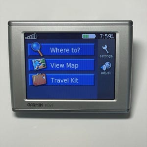 Può includere: Un dispositivo GPS Garmin nüvi argentato con touchscreen blu che mostra le opzioni di navigazione. Lo schermo mostra "Where to?", "View Map" e "Travel Kit". L'ora visualizzata è 19:59. Il dispositivo ha una forma rettangolare.