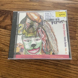 May include: A CD case featuring the album "George Clinton's Family Series Vol. 2." The cover art is a colorful illustration of a face with a dog-like appearance. The word "FUNK" is prominently displayed. A price tag is visible.