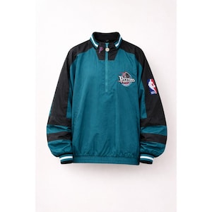 May include: Teal and black Detroit Pistons NBA team jacket. The jacket has a half-zip closure, a stand-up collar with white and purple stripes, and the Pistons logo on the chest. The sleeves are black, and the jacket has the NBA logo on the right sleeve.