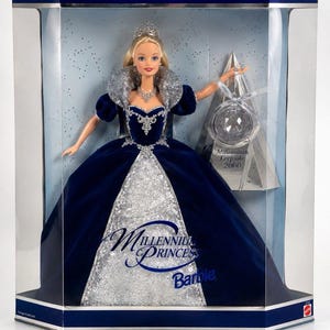 May include: A Millennium Princess Barbie doll in a display box, wearing a dark blue velvet gown with a silver glitter panel, a high collar, and a tiara. The doll holds a clear ornament labeled Millennium Keepsake 2000. The box text reads Special Millennium Edition.