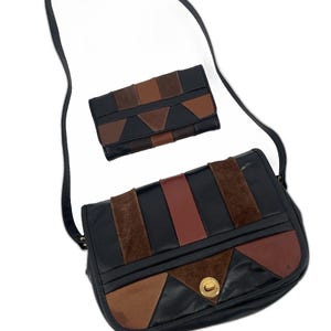 Puede incluir: Bolso de hombro negro y cartera a juego. El bolso presenta un diseño geométrico con paneles de cuero y ante negros, marrones y beige. El bolso tiene una correa larga negra y un cierre dorado. La cartera tiene un diseño geométrico similar.