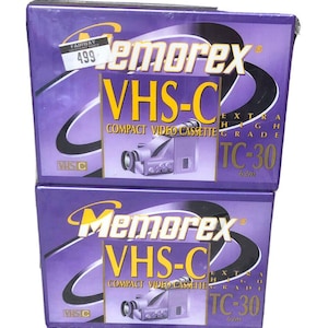 Könnte beinhalten: Zwei Memorex VHS-C TC-30 Kompakt-Videokassettenboxen. Die Boxen sind lila mit gelbem und weißem Text. Jede Box zeigt eine Grafik einer Videokamera. Die Boxen sind mit "Extra High Grade" beschriftet.