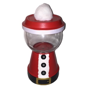 Peut inclure: Une machine à boules de gomme décorative en forme de Père Noël. Le haut rouge est orné d'un pompon blanc et d'un ruban blanc. La base rouge présente des boutons noirs et une ceinture noire avec une boucle dorée. Décoration de Noël amusante.