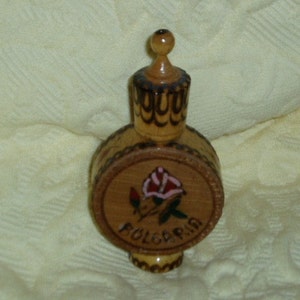 May include: A small wooden bottle with a rose design and the word "Bulgaria" carved into the side. The bottle has a wooden stopper and is decorated with intricate carvings.