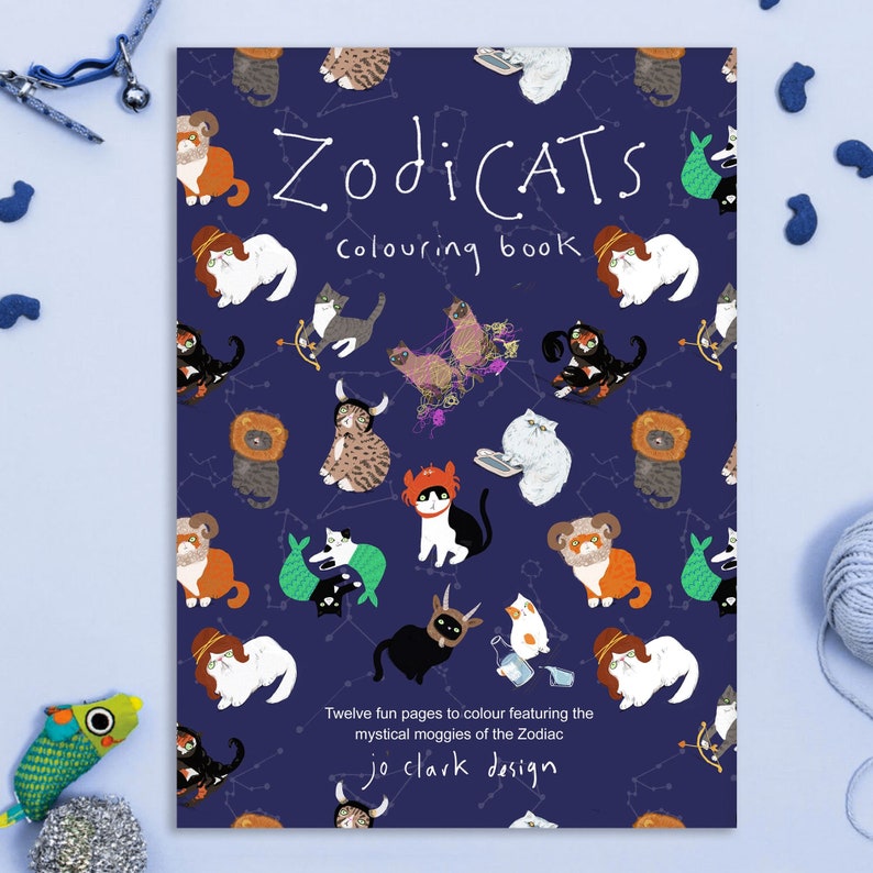 May include: A blue coloring book cover with a pattern of cats dressed as zodiac signs. The title is "ZodiCATS Coloring Book" and the text at the bottom reads "Twelve fun pages to color featuring the mystical moggies of the Zodiac jo clark design".