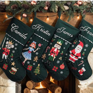 May include: Four dark green Christmas stockings featuring white embroidered names Camila, Kristin, James, and Frank. Each stocking displays festive appliqués including a mouse, a girl, a nutcracker, and Santa Claus, along with trees and gifts.