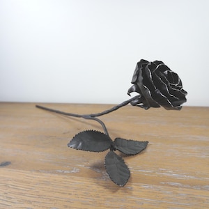 Puede incluir: Una rosa negra de metal con hojas, hecha de metal, sobre una superficie de madera.