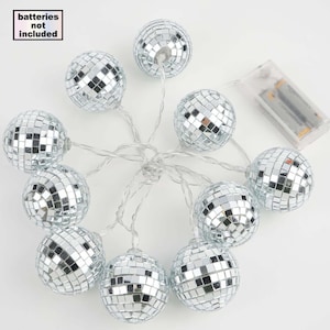 May include: A string of silver disco ball lights. The lights are arranged in a circular pattern, with each ball reflecting light. The text "batteries not included" is in the upper left corner. The lights are connected to a battery pack.
