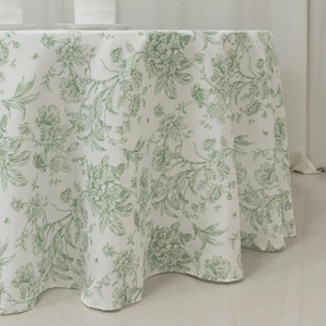 May include: A white round tablecloth with a green floral pattern. The design features detailed botanical illustrations of flowers and leaves. The tablecloth is made of a soft, flowing fabric, perfect for a dining table.