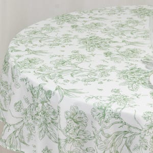 May include: A round white tablecloth with a green floral pattern. The design features detailed botanical illustrations of flowers and leaves, creating a classic and elegant aesthetic. The tablecloth is made of a smooth, likely woven, fabric.