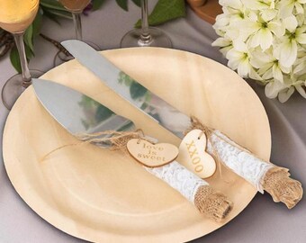 May include: A wedding cake knife and server set on a wooden plate. The handles are wrapped in burlap and lace, with wooden heart tags that read "love is sweet" and "XXOO".