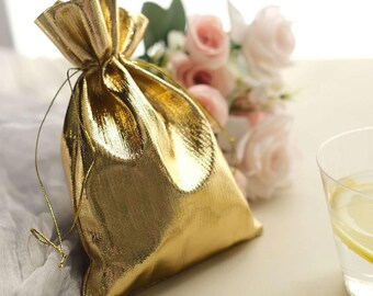 May include: A shiny gold drawstring gift bag with a textured surface. The bag is tied with a gold string and sits next to a bouquet of pink roses and a glass of water with lemon slices.