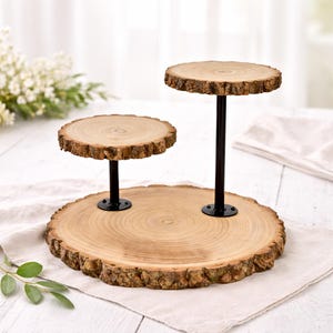 May include: A three-tiered wooden serving stand. The stand features three circular platforms made from natural wood slices with a rough bark edge. The platforms are supported by black metal posts and bases. The stand is on a neutral-colored surface.