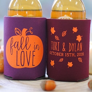 May include: Two purple and orange beverage insulators. One insulator has a pumpkin with the text "fall in love". The other insulator has the text "Tori & Dylan October 15th, 2016" with orange leaves.