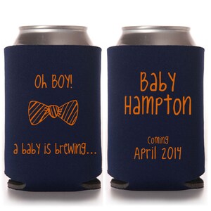 May include: Two navy blue can coolers with orange text. The first cooler says "Oh Boy! A baby is brewing..." with a cartoon bow tie. The second cooler says "Baby Hampton Coming April 2014".