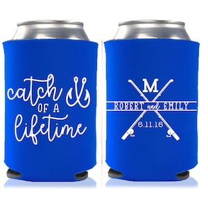 May include: Two blue can coolers with white text. One cooler says "catch of a lifetime" with a fishing hook. The other cooler has two crossed fishing rods with the text "Robert and Emily" and "M" in the center. The date "6.11.16" is below the names.