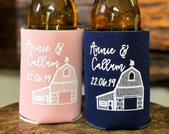 May include: Two foam bottle sleeves, one light pink and one navy blue, each featuring white screen-printed text that reads Annie & Callum and the date 22.06.19 above a line-art illustration of a barn with a weather vane on the roof.