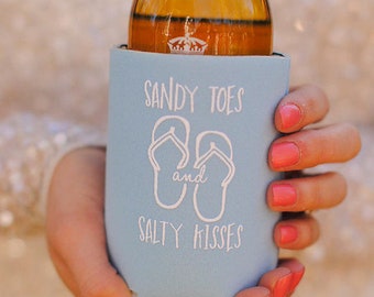 May include: A light blue can cooler with the text "Sandy Toes and Salty Kisses" and a graphic of two flip flops.