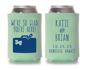May include: Two green and white can coolers with text. The left cooler says "We're so glad you're here!" with a blue suitcase icon. The right cooler says "Katie and Brian 10.25.15 Honolulu, Hawaii".