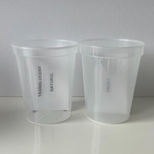 Op de afbeelding: Twee doorzichtige plastic bekers, een met het label "TRANSLUCENT NATURAL" en de andere met het label "FROST".