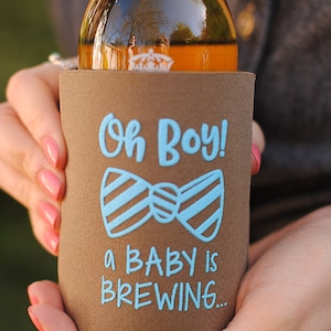 May include: A brown beverage insulator with a blue bow tie and the text "Oh Boy! A Baby is Brewing..."