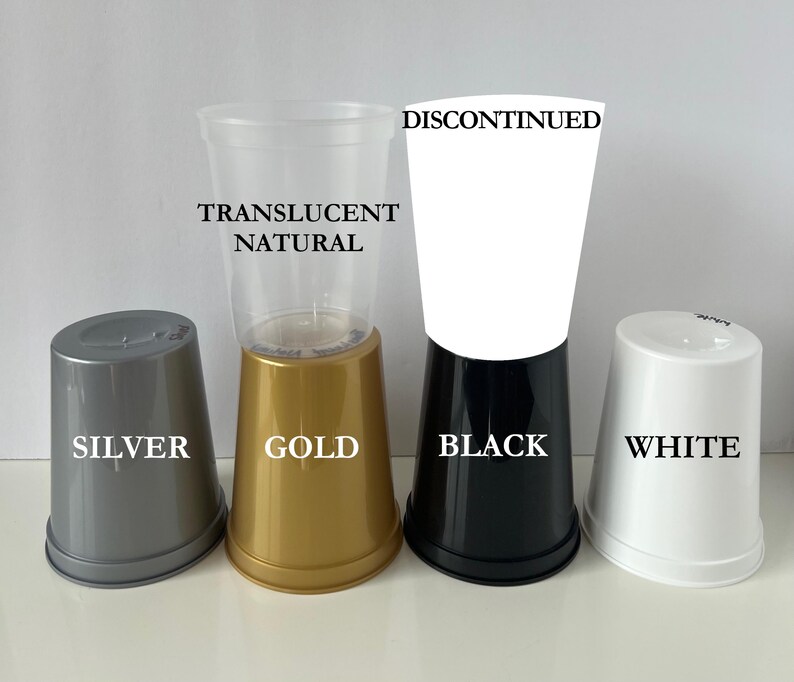 Op de afbeelding: Een verzameling plastic bekers in verschillende kleuren, waaronder zilver, goud, zwart en wit, samen met een doorzichtige natuurlijke beker. Tekstlabels identificeren de kleuren en geven aan dat de witte beker niet meer leverbaar is.