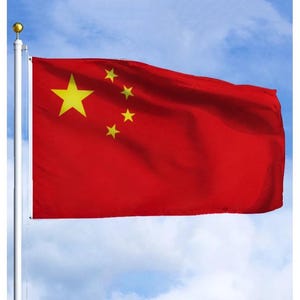 Puede incluir: Una bandera roja con una gran estrella amarilla y cuatro estrellas amarillas más pequeñas en la esquina superior izquierda, ondeando al viento contra un cielo azul. La bandera está sujeta a un mástil blanco.