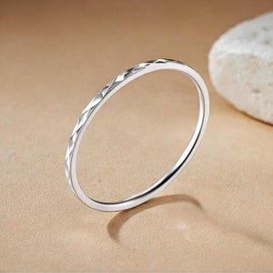 Op de afbeelding: Een dunne zilveren ring met een getextureerd diamantpatroon.
