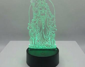 Puede incluir: Una lámpara de acrílico iluminada con la figura grabada de una deidad sosteniendo una antorcha, flanqueada por dos lobos, dentro de un marco arqueado. El diseño brilla con una luz verde brillante y se monta sobre una base negra circular.