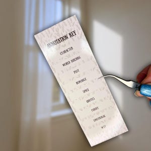 May include: A rectangular white annotation key with the title "ANNOTATION KEY" and categories like "CHARACTER" and "WORLD BUILDING". The key is held by tweezers against a neutral background.