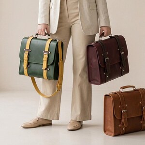 Women's leather messenger bag in dark green with yellow straps, burgundy, and tan brown full grain leather, held by a woman in a beige linen suit. Handcrafted leather briefcase for women available in 4 sizes: small, medium, large, XL. Leather satchel bag with double buckle closure, top handle, detachable crossbody strap, and metal rivet details. Personalized leather work bag, laptop bag women, leather office bag, gift for her