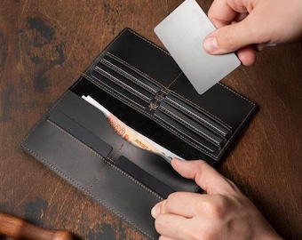 May include: A long, black leather wallet featuring multiple horizontal card slots, a large open compartment containing a banknote, and a smooth matte finish. The wallet is open, revealing its interior structure with visible stitching along the edges.