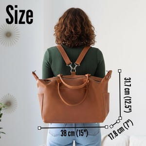May include: A tan brown convertible backpack with two top handles and a zippered main compartment. The bag measures 15 inches wide, 12.5 inches high, and 7 inches deep. It features adjustable shoulder straps attached to a central metal ring.