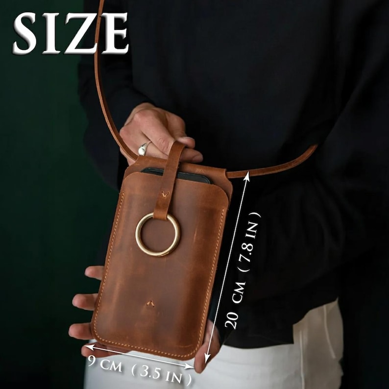 May include: A brown leather phone pouch with a long shoulder strap and a prominent gold-toned metal ring closure on the front. The pouch measures 20 cm (7.8 inches) in height and 9 cm (3.5 inches) in width, as indicated by the text on the image.