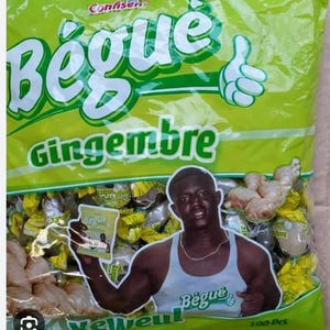 May include: A green bag of Bègue Ginger sweets. The bag features a cartoon hand giving a thumbs up and a man holding a smaller bag of the sweets. The bag contains 100 pieces.