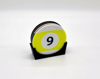 May include: A set of round coasters featuring a billiards theme. Each coaster displays a yellow and white design with the number 9 in black. The coasters are held in a black, angled holder.