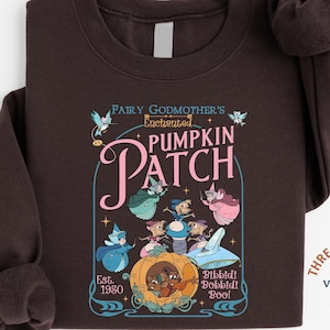 May include: Dark chocolate-colored sweatshirt featuring a graphic of the Fairy Godmother's Enchanted Pumpkin Patch. The design includes illustrations of fairy godmothers, mice, and a pumpkin carriage. Text includes "Est. 1980" and "Bibbidi Bobbidi Boo!"