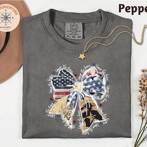 a gray t-shirt with a patriotic design, including a bow and stars, along with a necklace and a hat.