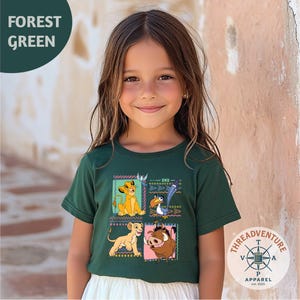 May include: A forest green short-sleeve t-shirt featuring a graphic print of four characters from The Lion King, including Simba, Zazu, and Pumbaa, arranged in a grid with colorful geometric patterns and borders on the front of the garment.