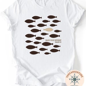 A white t-shirt with a graphic design featuring a group of fish and a single fish in a unique position, along with the text "Called to be Different Romano 122".