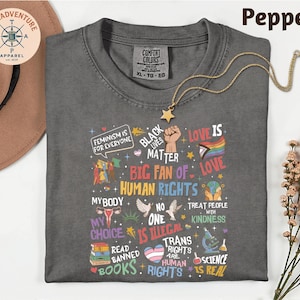 a gray t-shirt with a variety of colorful text and graphics printed on it, along with a necklace and a hat.